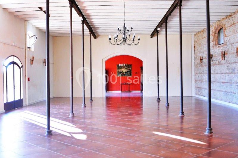 Salle spacieuse avec sol en carrelage, murs clairs, piliers métalliques, lustre central et alcôve rouge au fond.