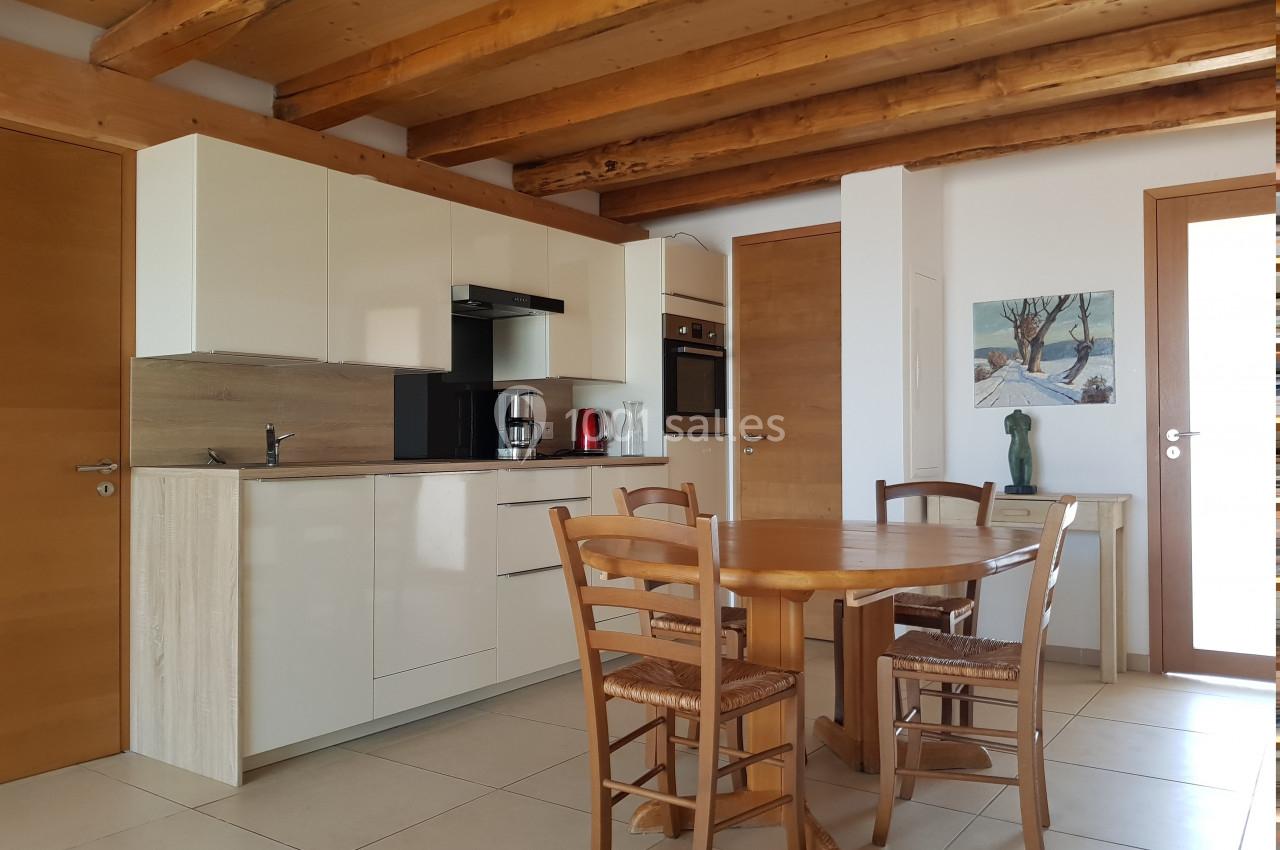 Cuisine moderne avec meubles en bois clair, table ronde et chaises, poutres apparentes au plafond.