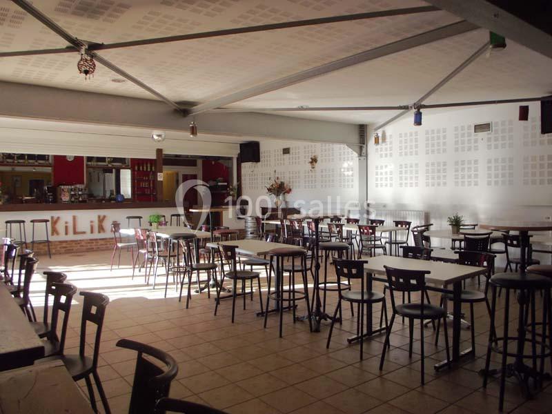 Salle lumineuse avec tables et chaises hautes disposées autour d'un bar en arrière-plan.