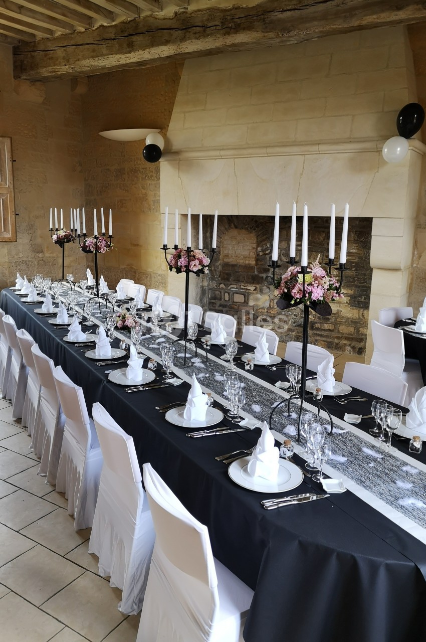Grande table de réception élégamment dressée avec nappes noires, chandeliers, fleurs et serviettes pliées, dans une salle en…