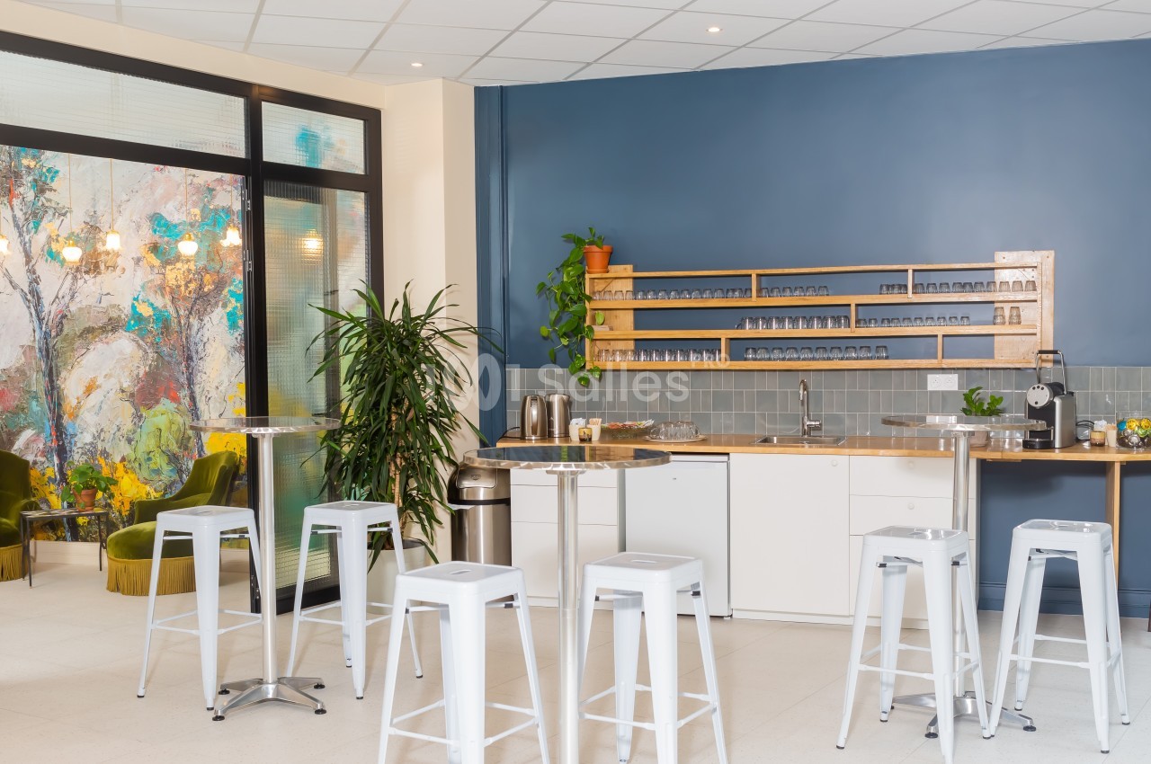 Cuisine moderne avec comptoir, tabourets hauts blancs, étagères en bois, plantes et mur bleu en arrière-plan.