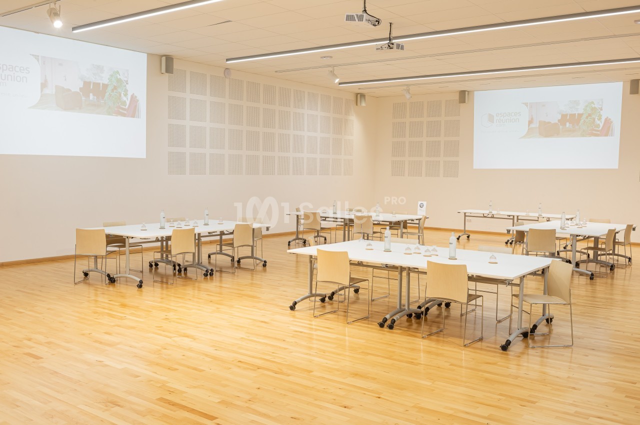 Salle de réunion lumineuse avec parquet, tables modulables, chaises en bois clair et projecteurs au plafond.