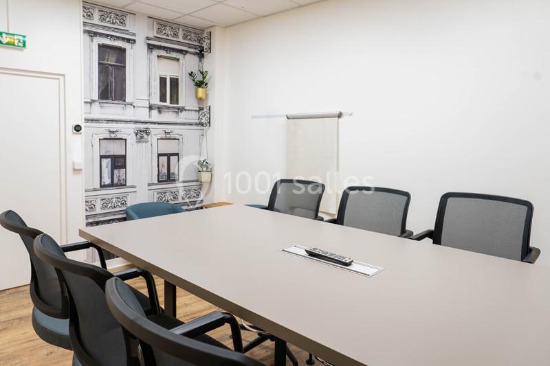 Salle de réunion lumineuse avec une grande table, des chaises noires et un mur décoré d'une photo de façade urbaine.
