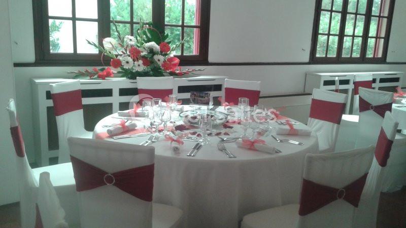 Table ronde dressée pour un événement, décorée de nappes blanches, nœuds rouges et centre de table floral.
