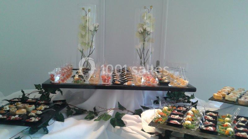 Buffet élégant avec verrines et amuse-bouches variés, décoré de feuillage et de fleurs blanches en arrière-plan.
