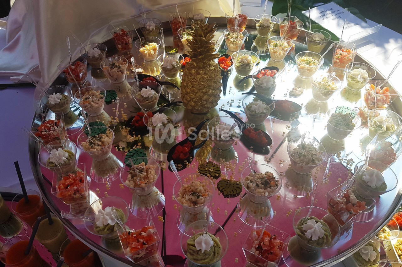 Plateau circulaire avec verrines variées, décoré d'un ananas doré au centre, présenté sur une table.