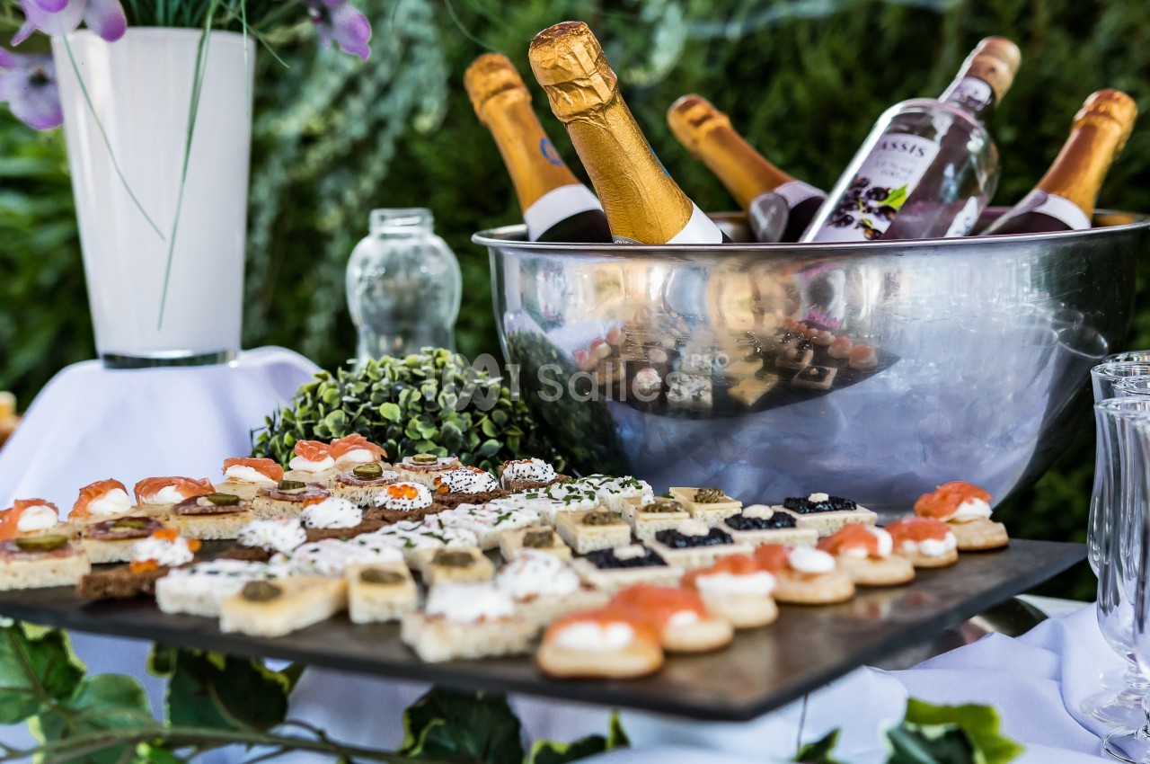 Plateau de canapés variés devant un seau rempli de bouteilles de champagne et de vin, décoré de verdure.