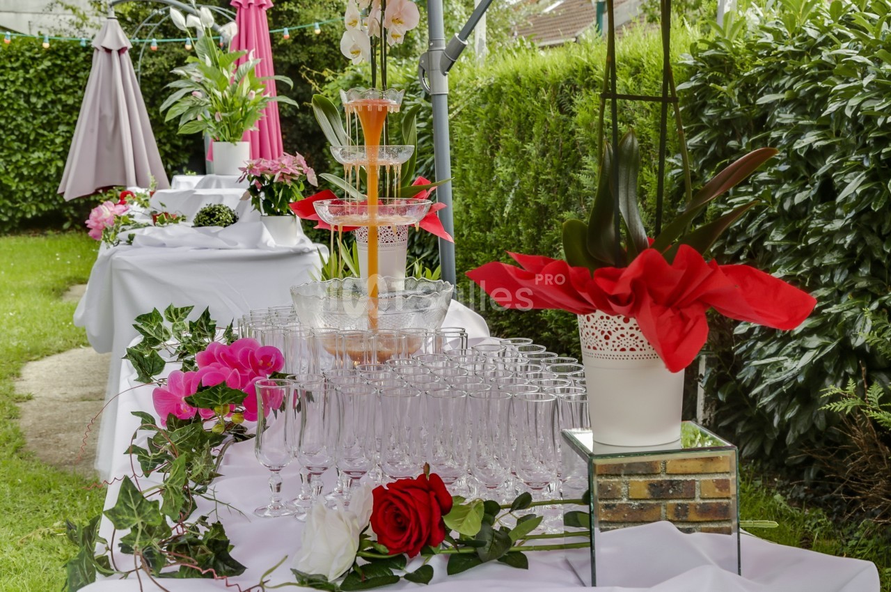 Table décorée en extérieur avec fontaine à boisson, verres alignés, plantes et fleurs colorées.