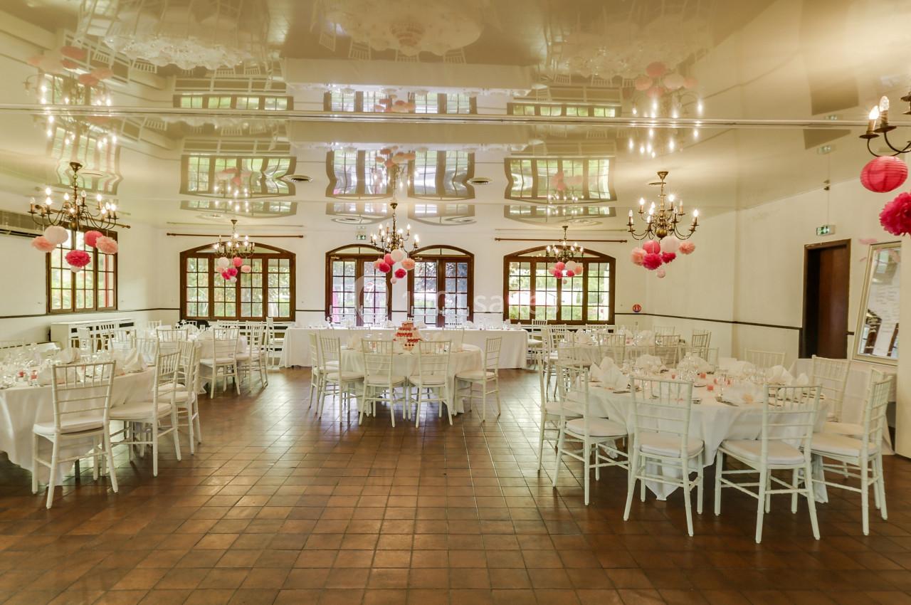 Salle de réception décorée avec des tables rondes, des chaises blanches et des lanternes roses suspendues au plafond.