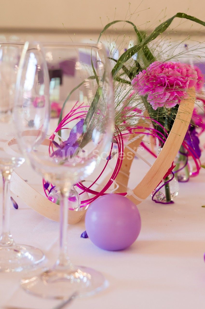 Centre de table floral avec des fleurs roses, éléments décoratifs en bois et une boule violette, sur une table dressée.