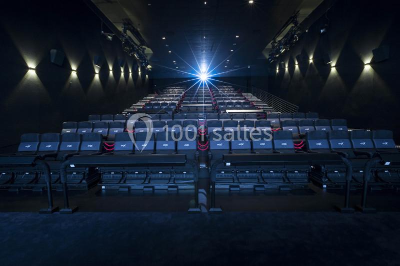 Salle de cinéma vide avec rangées de sièges inclinables et un projecteur allumé au fond.