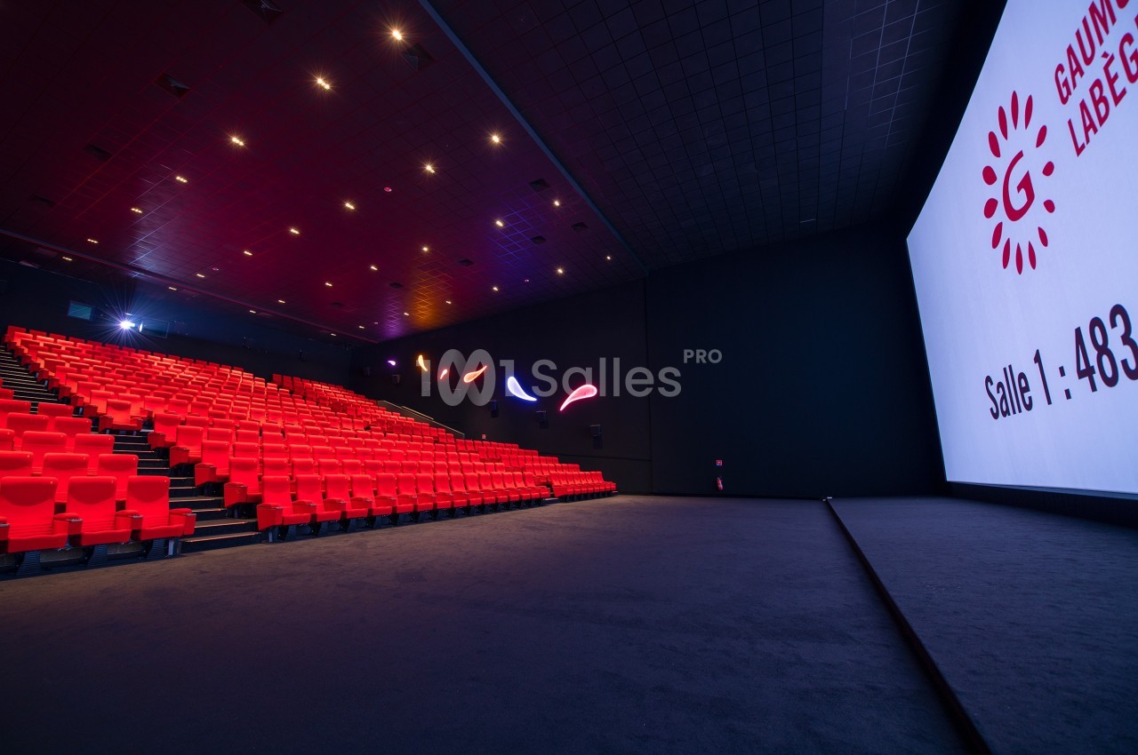 Salle de cinéma vide avec sièges rouges, grand écran affichant ’Salle 1 : 483 places’ et éclairage tamisé.