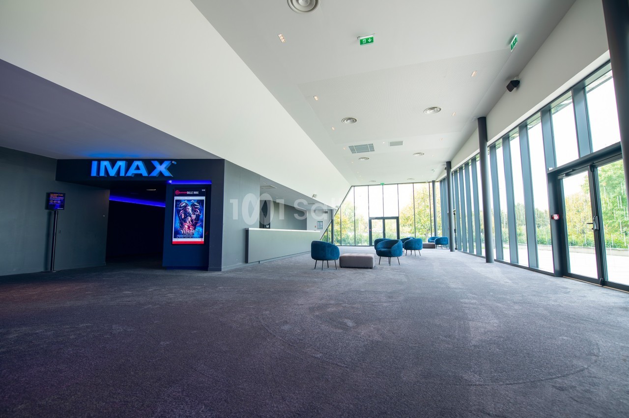 Hall d'entrée spacieux avec moquette, fauteuils, grandes baies vitrées et accès à une salle IMAX illuminée.