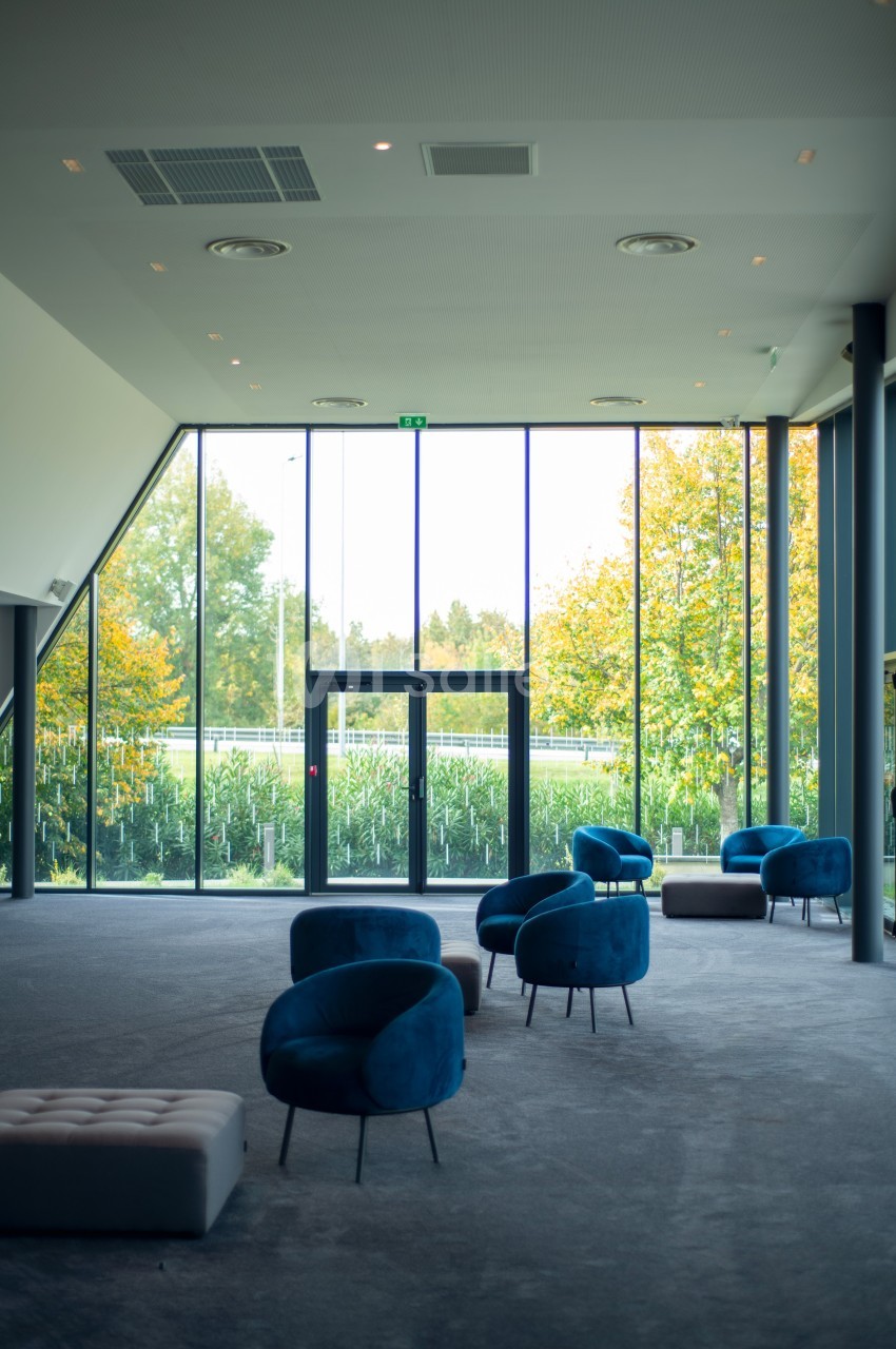 Salle lumineuse avec de grandes baies vitrées, des fauteuils bleus et une vue sur un jardin verdoyant.