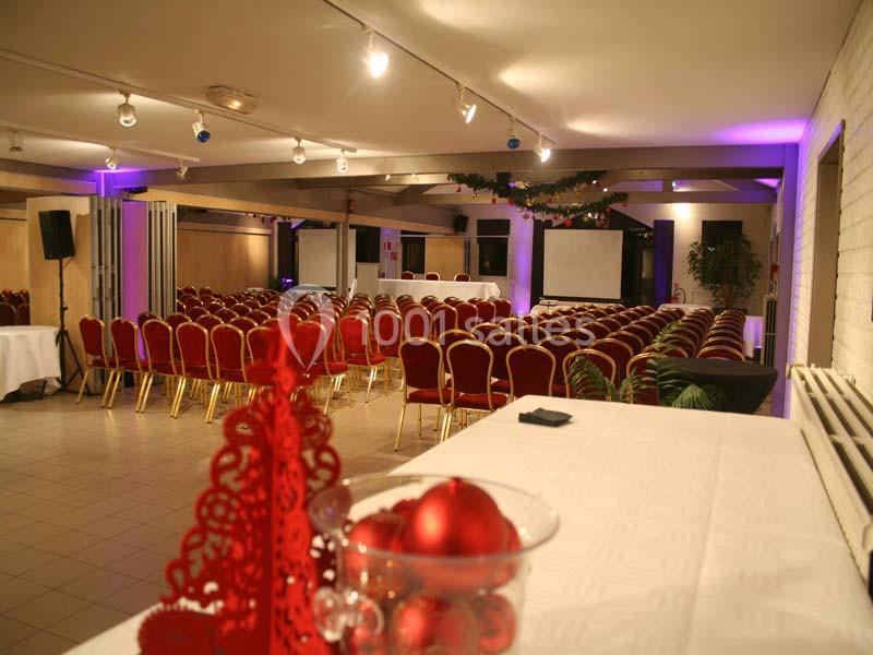Salle de conférence décorée avec des chaises rouges alignées, une table blanche et des décorations de Noël au premier plan.
