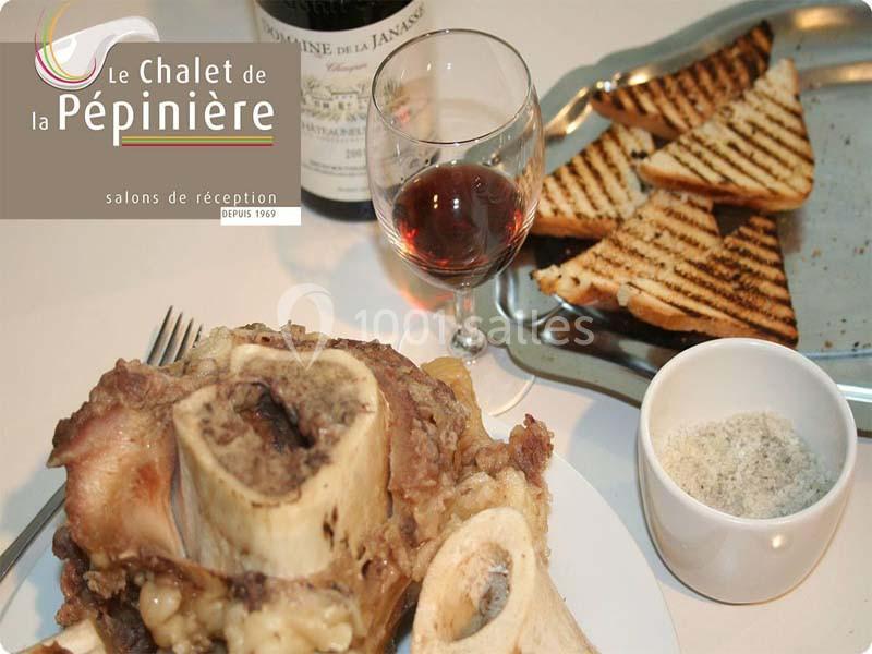 Assiette d'os à moelle avec pain grillé, verre de vin rouge et sel, posés sur une table avec une bouteille en arrière-plan.