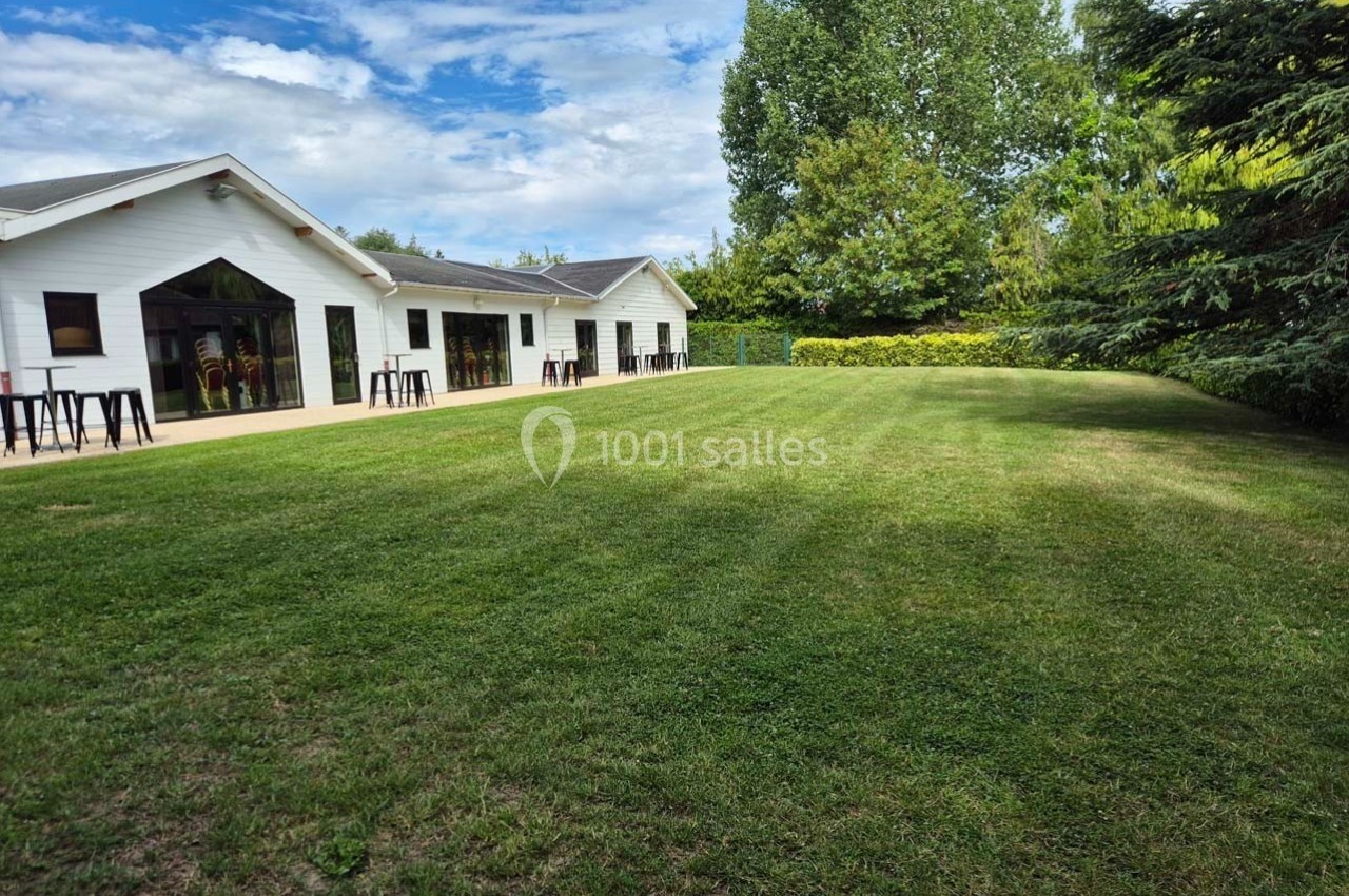 Pelouse bien entretenue devant un bâtiment blanc avec de grandes baies vitrées, entouré d'arbres et de haies.