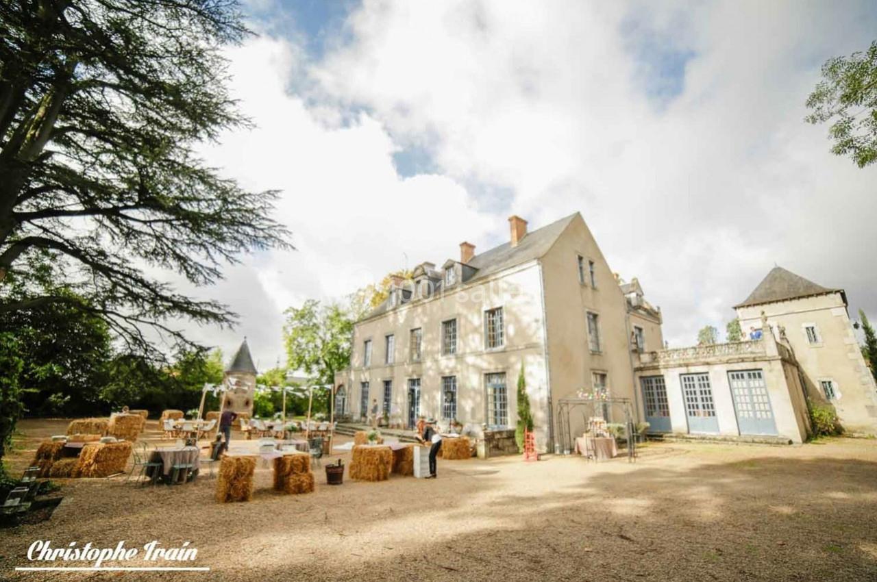 Grande maison de campagne en pierre avec des tables et bottes de foin disposées dans une cour ensoleillée.