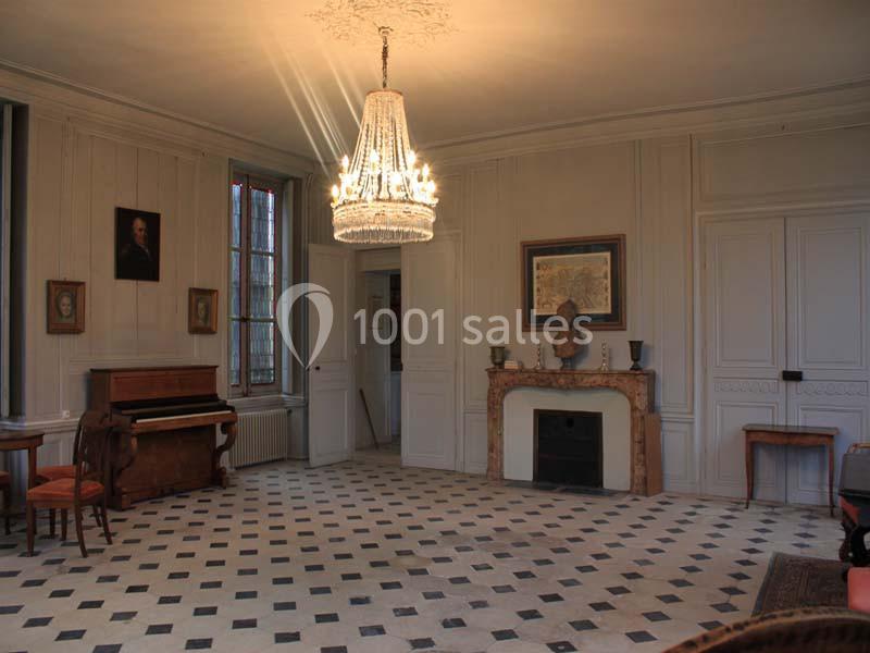 Salle lumineuse avec un lustre, un piano, une cheminée en marbre et un sol en damier noir et blanc.