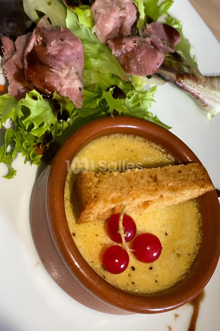 Crème brûlée servie avec un croûton, des groseilles et une salade verte accompagnée de tranches de viande.