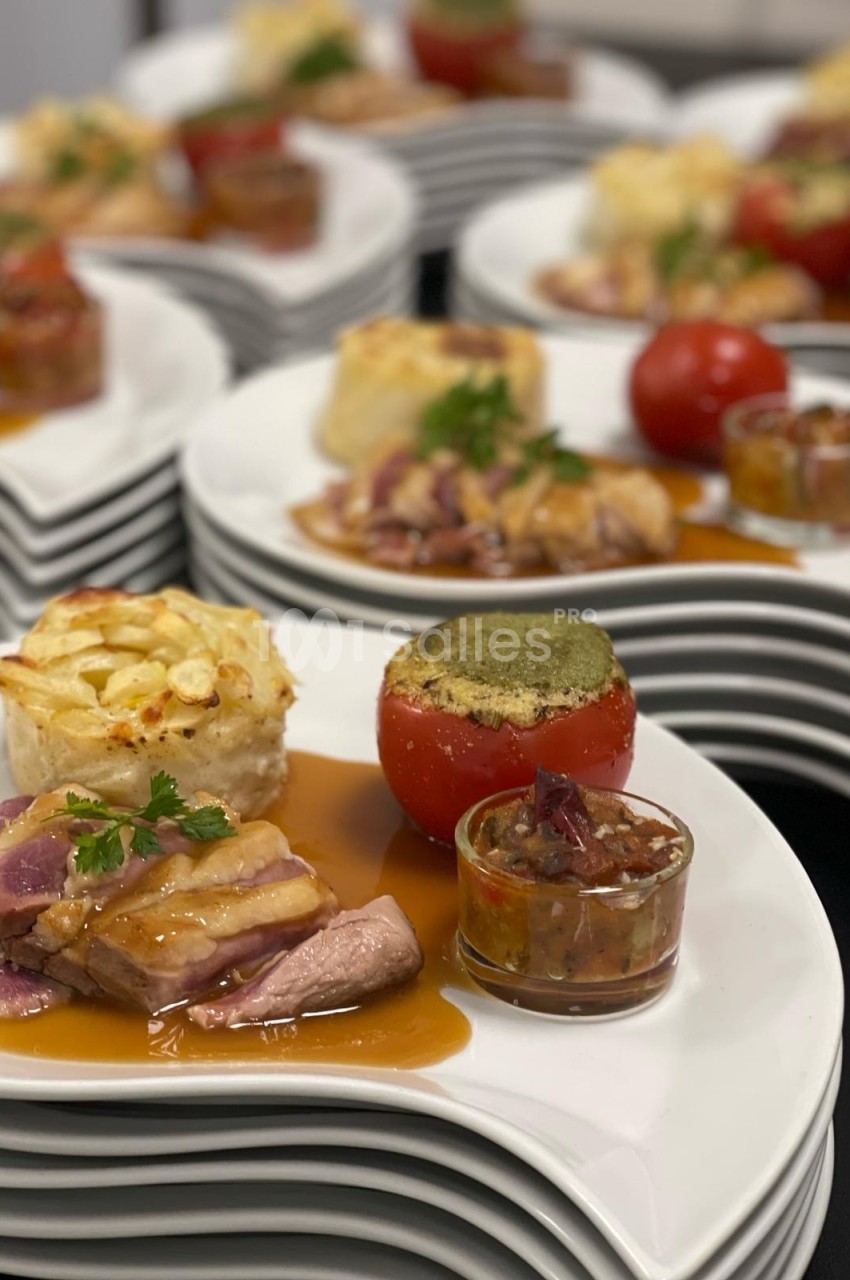 Assiettes dressées avec viande en sauce, gratin, tomate farcie et accompagnements, présentées sur des plats blancs empilés.