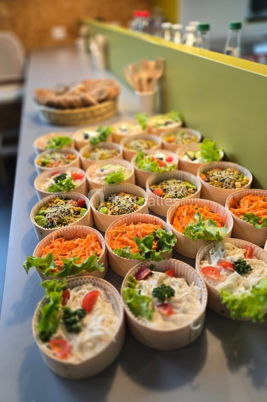 Assortiment de plats froids individuels présentés dans des bols en carton, garnis de légumes frais et colorés.