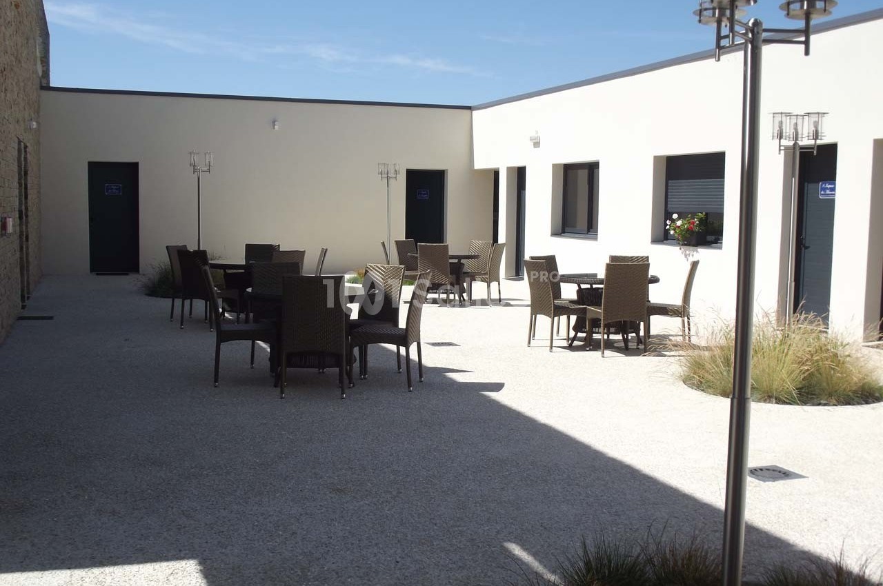 Cour intérieure avec mobilier de jardin en rotin, entourée de murs clairs et éclairée par un ciel dégagé.