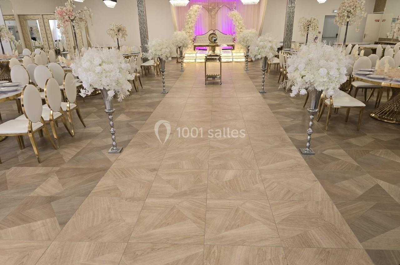 Salle de réception décorée avec des chaises blanches, des tables dressées et des arrangements floraux blancs.