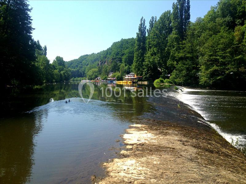 Rivière bordée d'arbres avec un petit barrage et des pédalos colorés amarrés au loin.