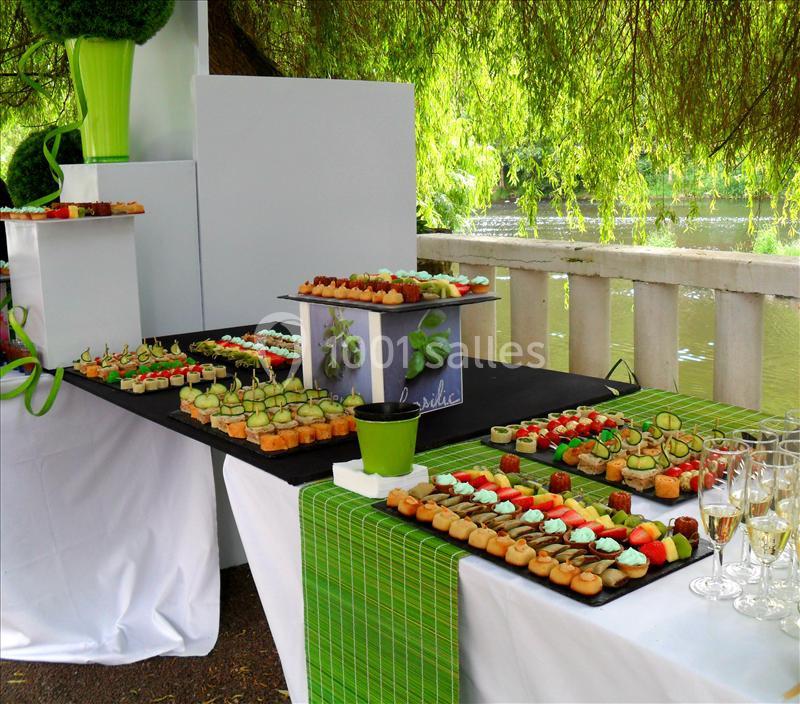 Buffet en plein air avec des plateaux de petits fours colorés, disposés sur des nappes vertes près d'un plan d'eau.