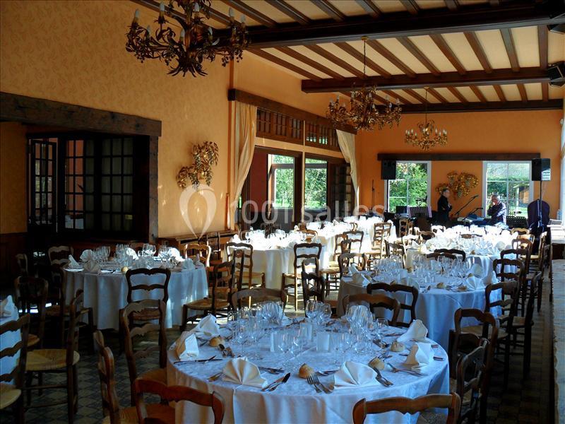 Salle de réception lumineuse avec tables rondes dressées, nappes blanches et chaises en bois, décor rustique et élégant.
