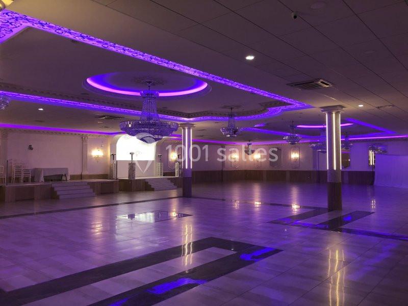 Salle de réception spacieuse avec sol en marbre, lustres imposants et éclairage violet au plafond.