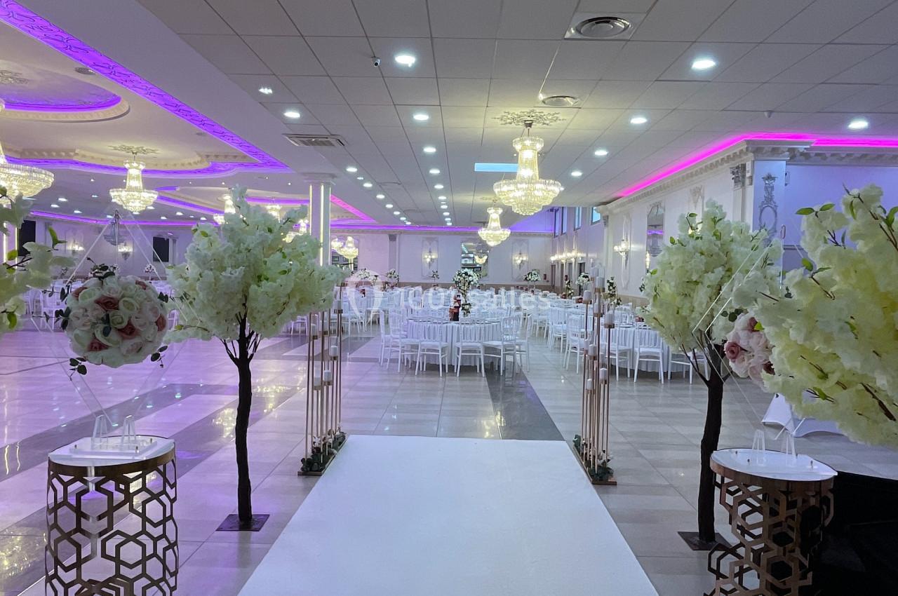 Allée centrale décorée de fleurs blanches menant à une salle de réception lumineuse avec des lustres suspendus.