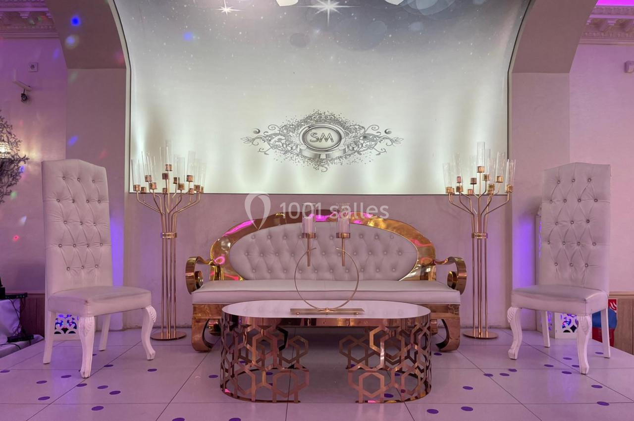 Salon élégant avec canapé blanc capitonné, deux chaises assorties, table basse dorée et décor lumineux en arrière-plan.