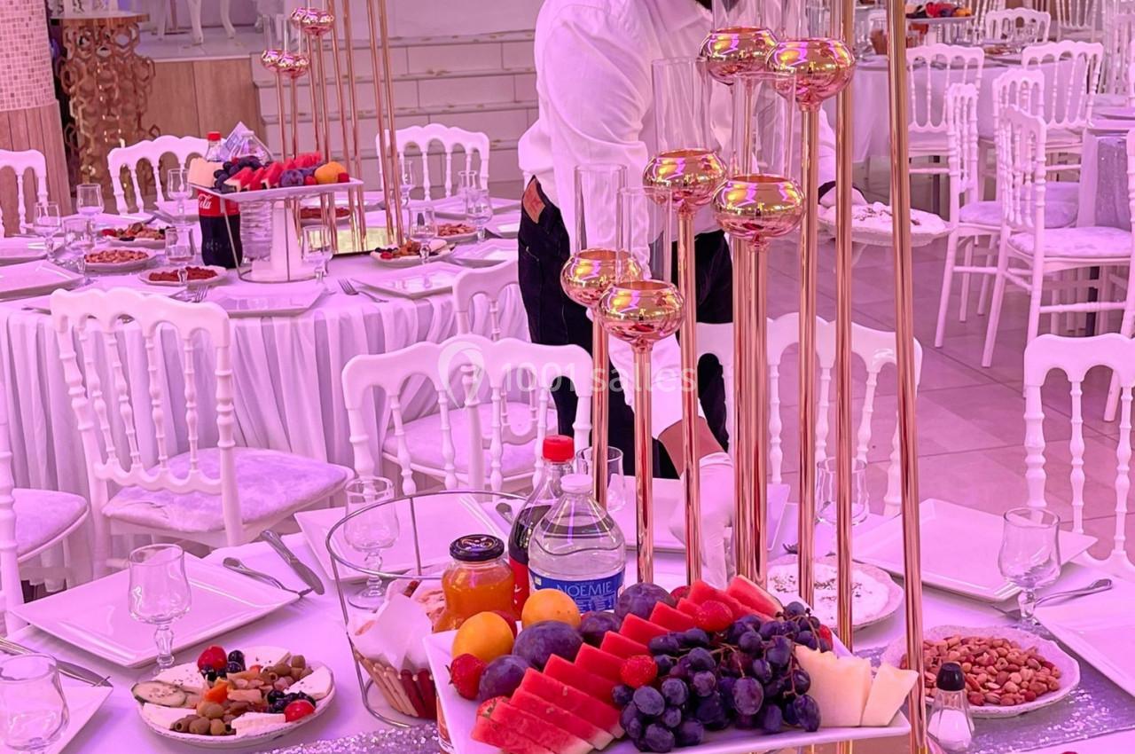 Un serveur prépare une table élégamment dressée avec des fruits, des plats variés et des chandeliers dorés.