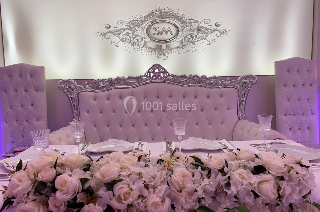 Table de réception élégamment décorée avec des fleurs blanches, vaisselle raffinée et canapé capitonné en arrière-plan.