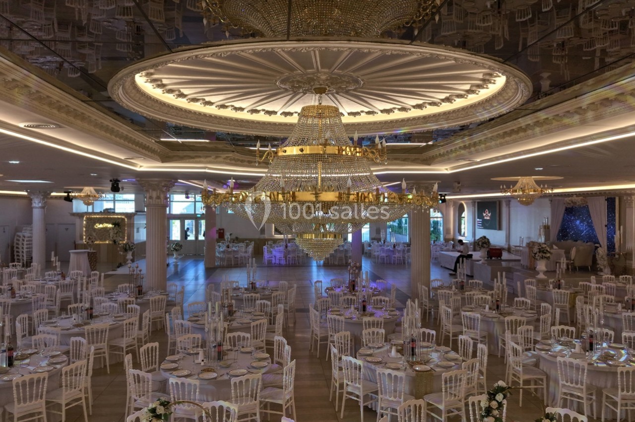 Salle de réception élégante avec de grandes tables dressées et un imposant lustre central en cristal.