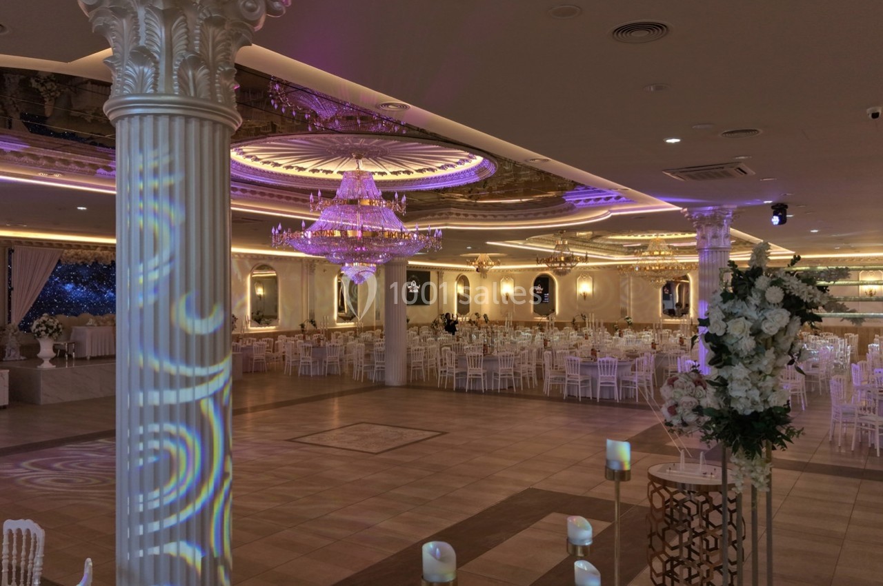 Salle de réception élégante avec lustres, colonnes décoratives, tables dressées et éclairage tamisé.