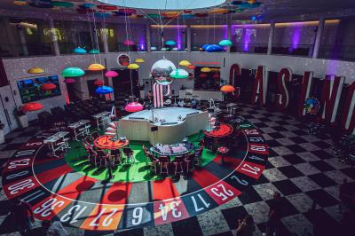 Salle de réception avec tables dressées, verres alignés au premier plan et décorations florales en arrière-plan.