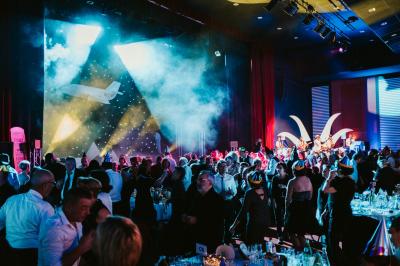 Salle de réception avec tables dressées, verres alignés au premier plan et décorations florales en arrière-plan.