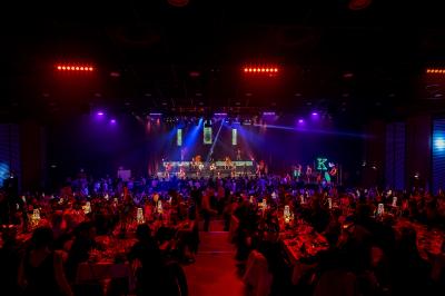 Salle de réception avec tables dressées, verres alignés au premier plan et décorations florales en arrière-plan.