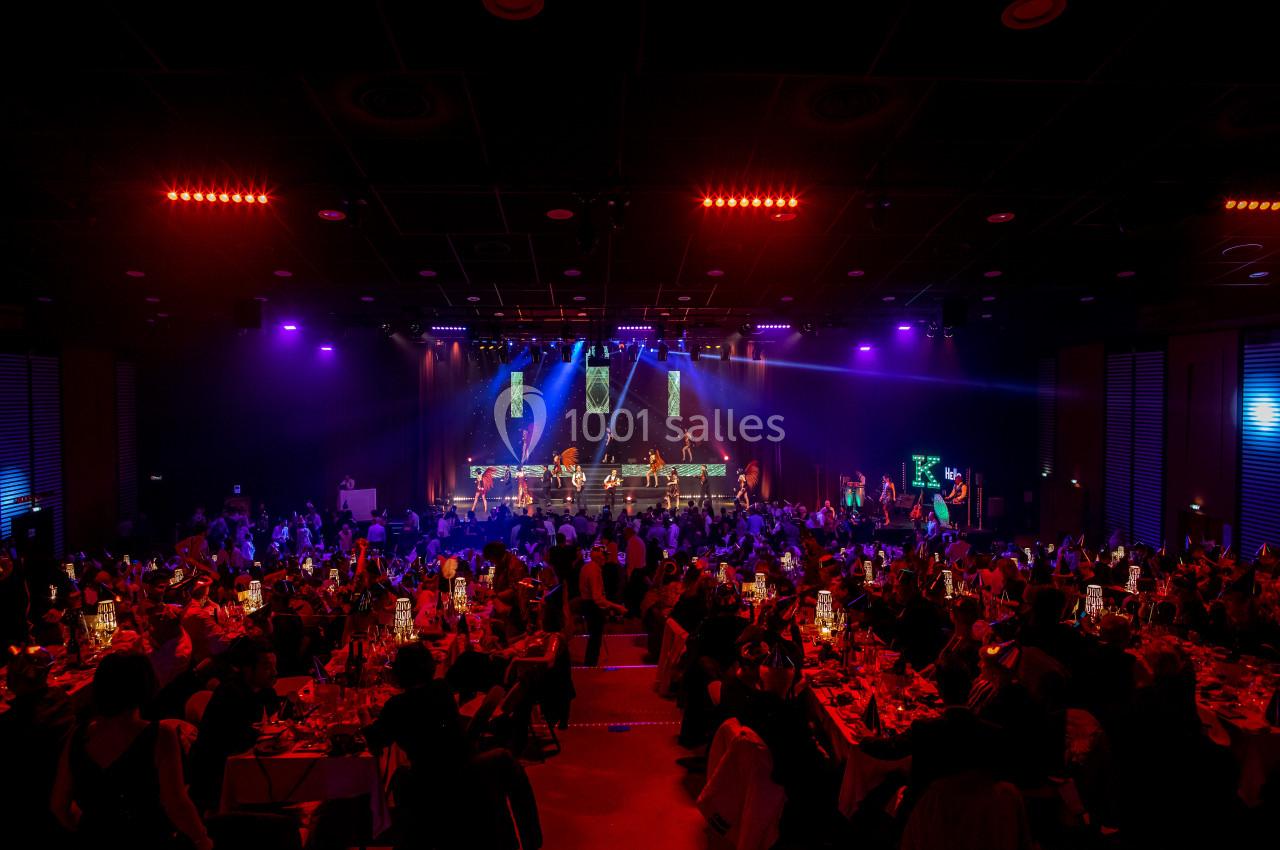Salle de spectacle illuminée avec des invités assis à des tables, face à une scène animée par des musiciens.