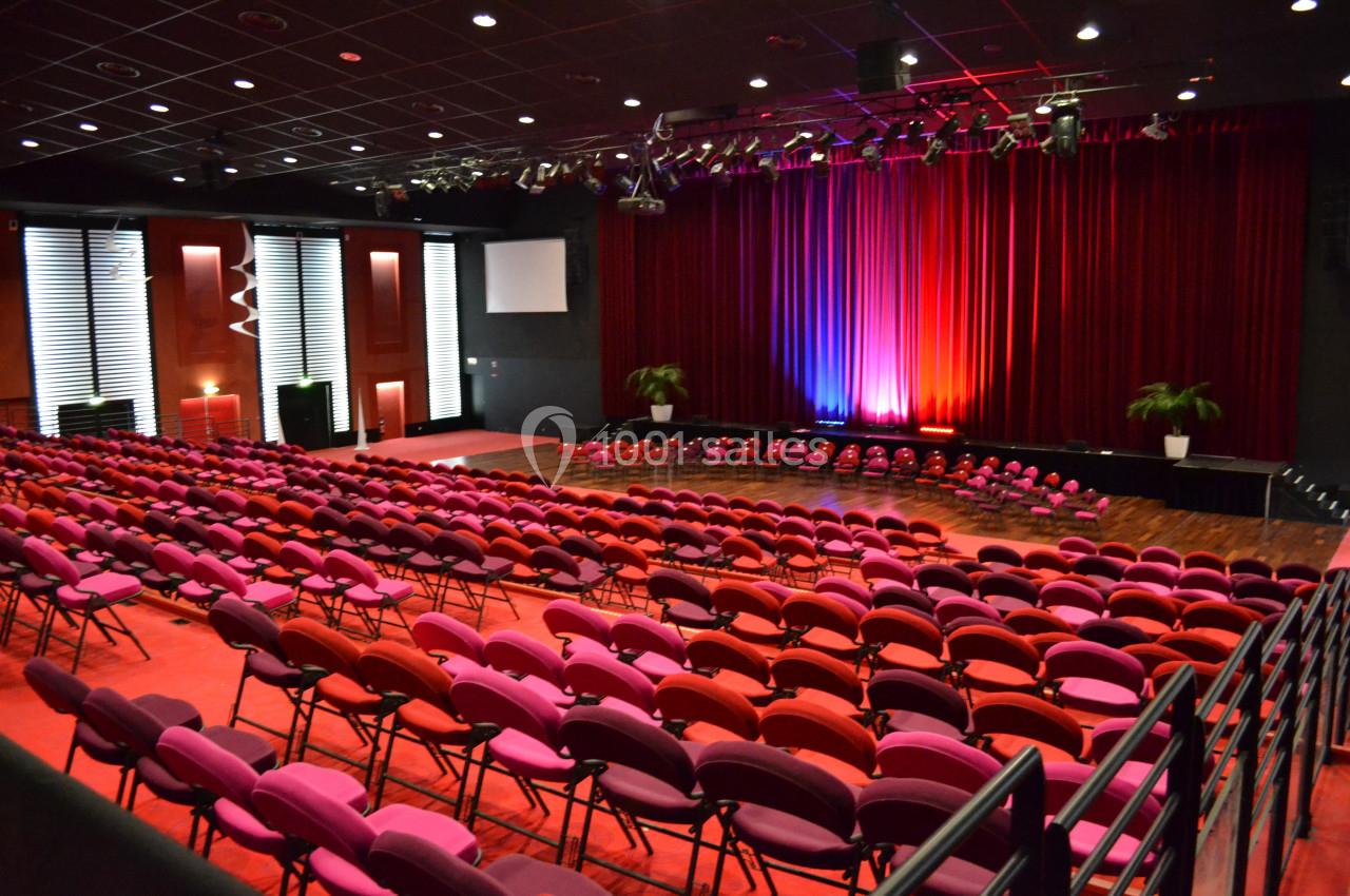 Location salle La Grande-Motte (Hérault) - Pasino de la Grande Motte #4 Salle de spectacle avec rangées de sièges rouges et roses, scène éclairée par des lumières colorées et rideaux rouges.