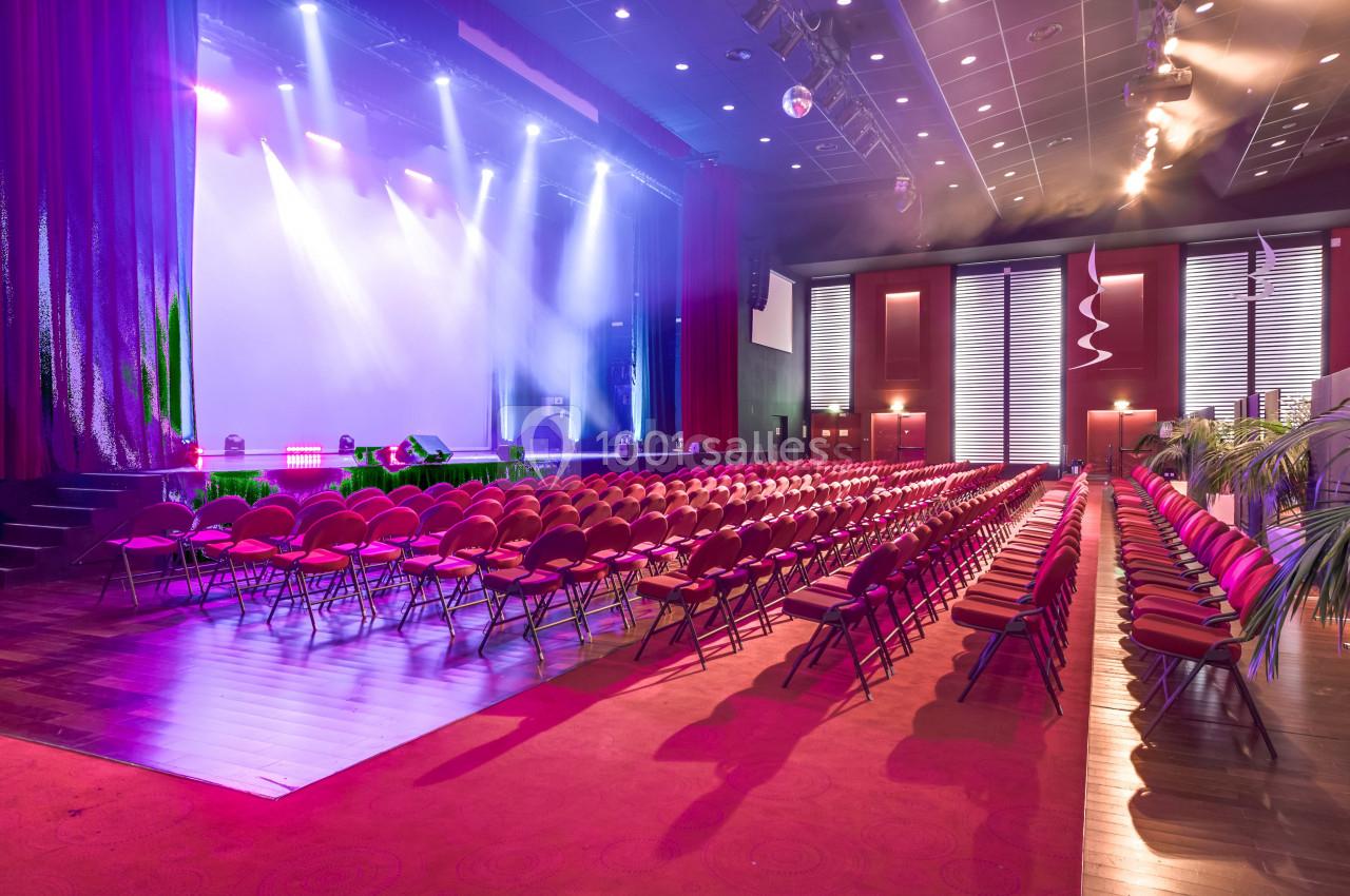 Location salle La Grande-Motte (Hérault) - Pasino de la Grande Motte #8 Salle de spectacle avec rangées de sièges rouges, scène éclairée par des projecteurs et rideaux ouverts.