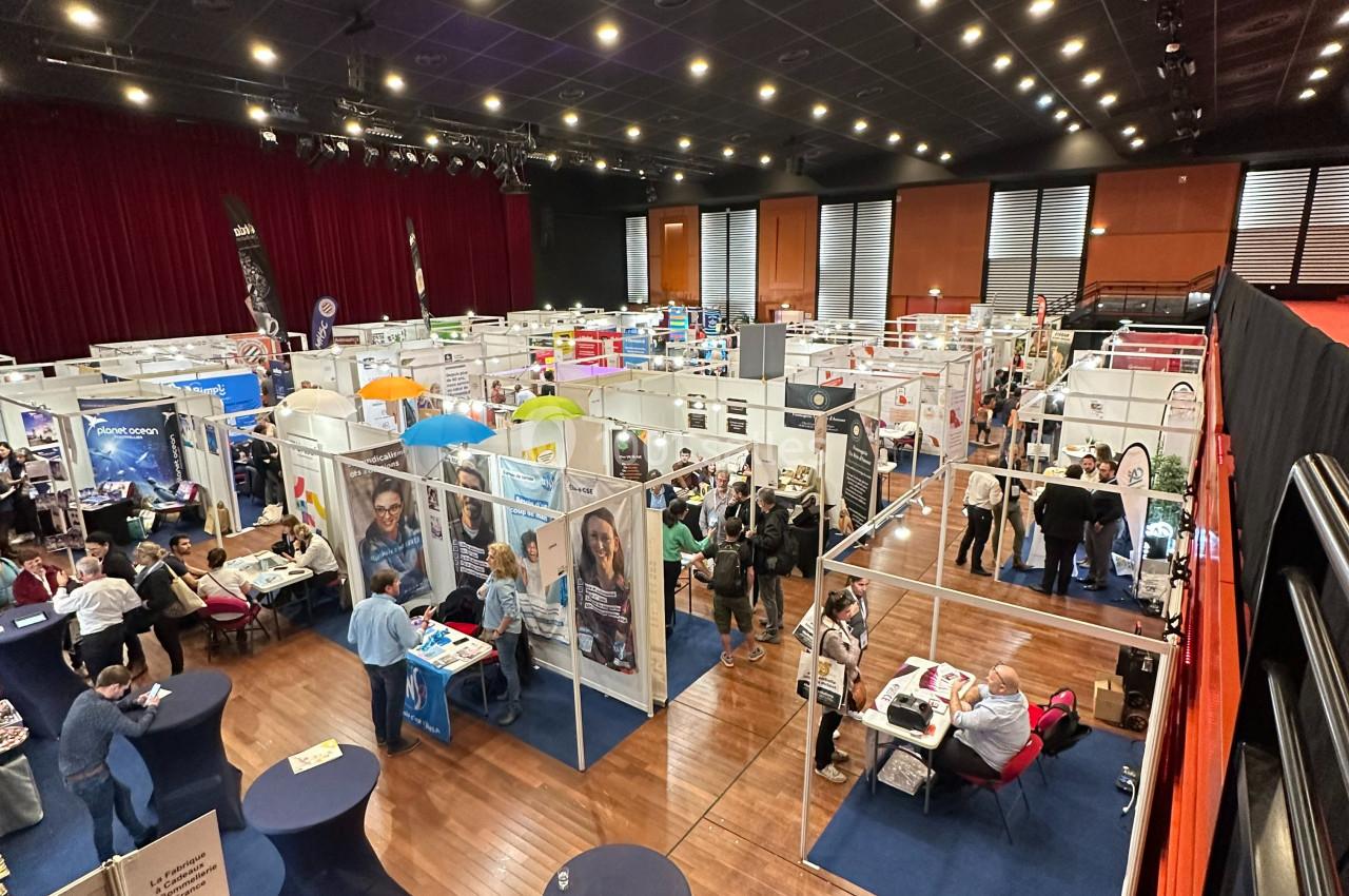 Location salle La Grande-Motte (Hérault) - Pasino de la Grande Motte #5 Vue d'ensemble d'un salon professionnel avec des stands, des visiteurs et une scène dans une grande salle éclairée.