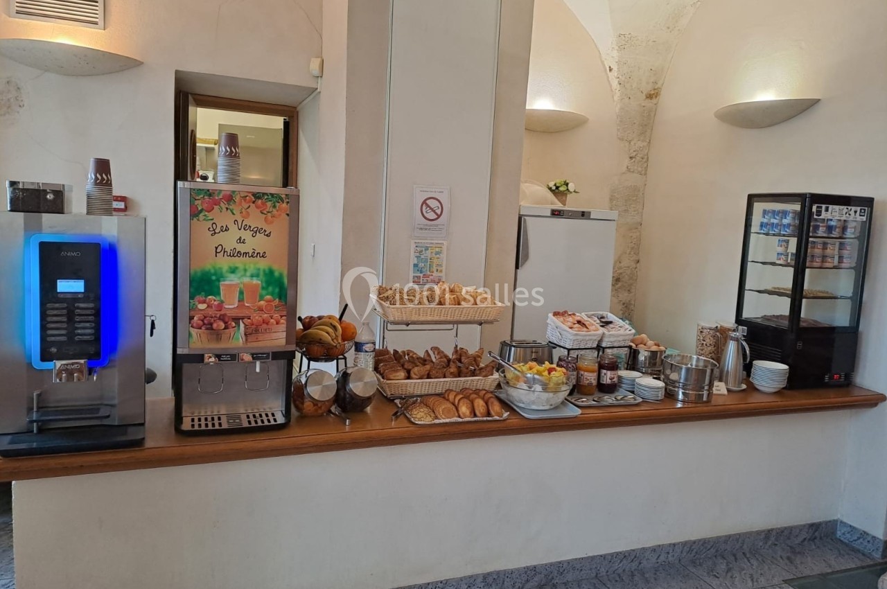 Buffet de petit-déjeuner avec machine à café, viennoiseries, fruits, céréales et produits frais dans une salle lumineuse.