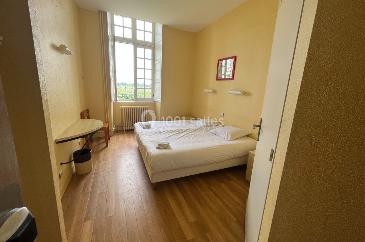 Chambre lumineuse avec deux lits simples, parquet au sol, bureau, chaise et grande fenêtre donnant sur l'extérieur.