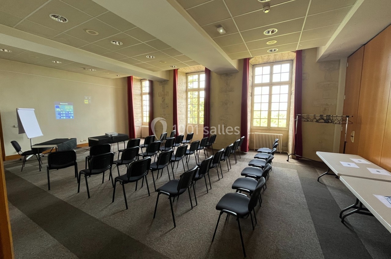 Salle de réunion lumineuse avec des rangées de chaises, un tableau de conférence, un projecteur et des tables sur les côtés.