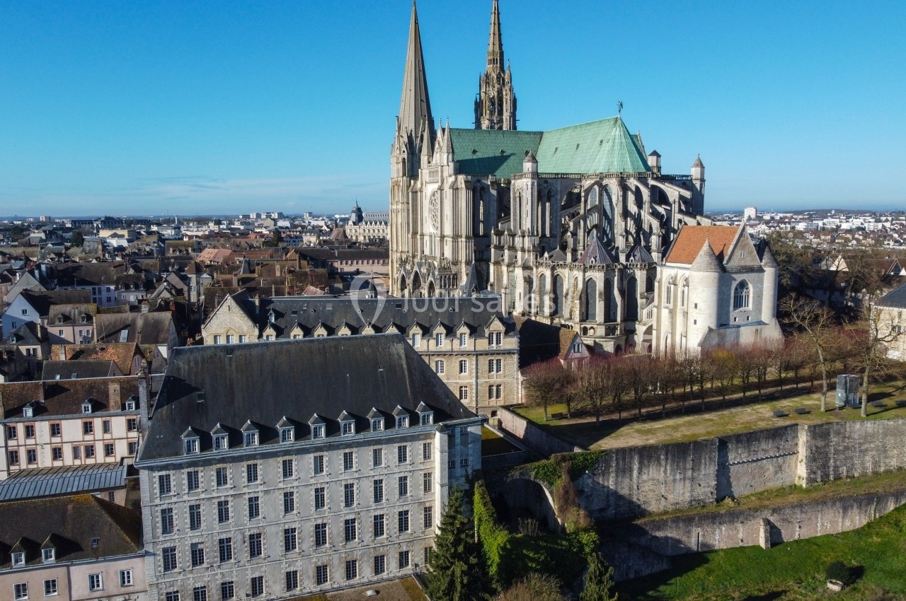 Vue aérienne de la cathédrale de Chartres entourée de bâtiments historiques et de jardins sous un ciel bleu.