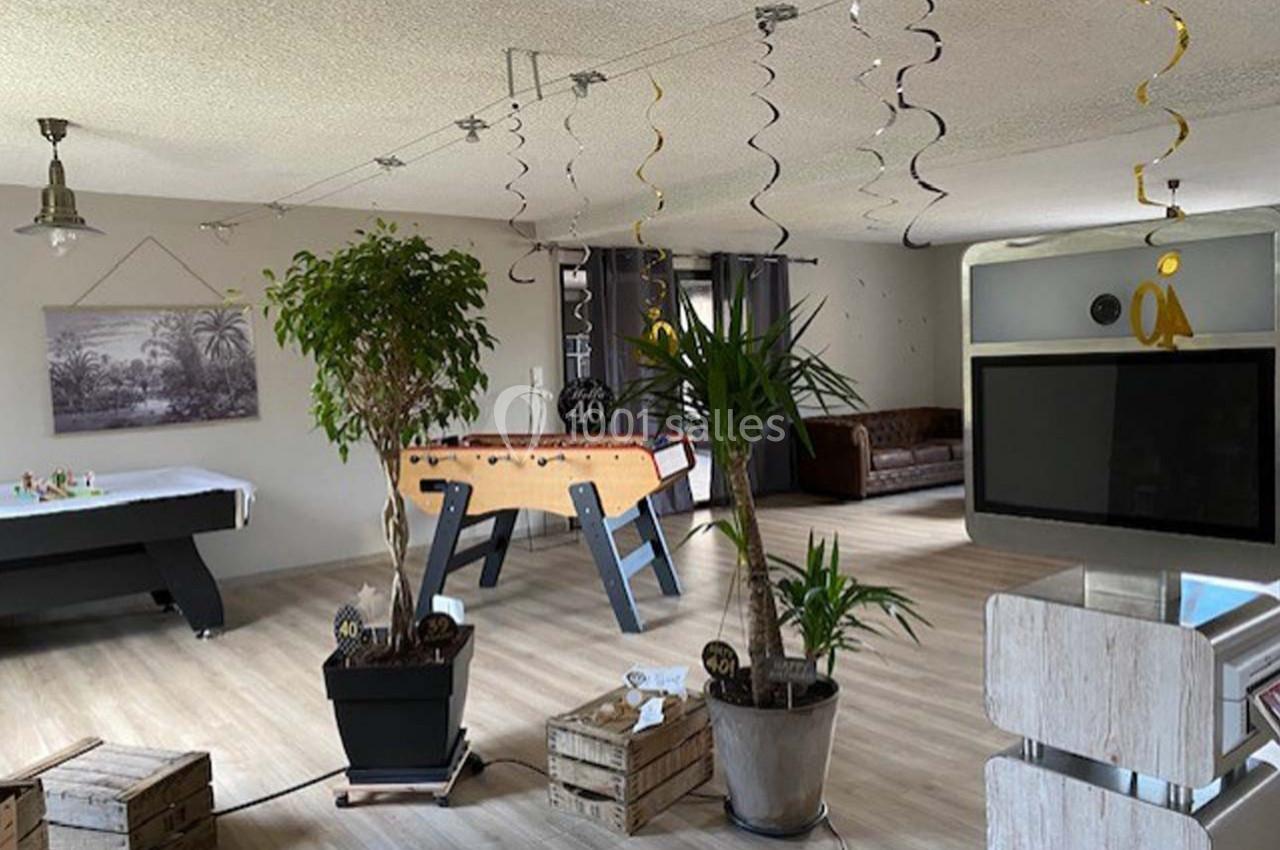 Salle de loisirs lumineuse avec baby-foot, billard, plantes en pot et décorations suspendues.